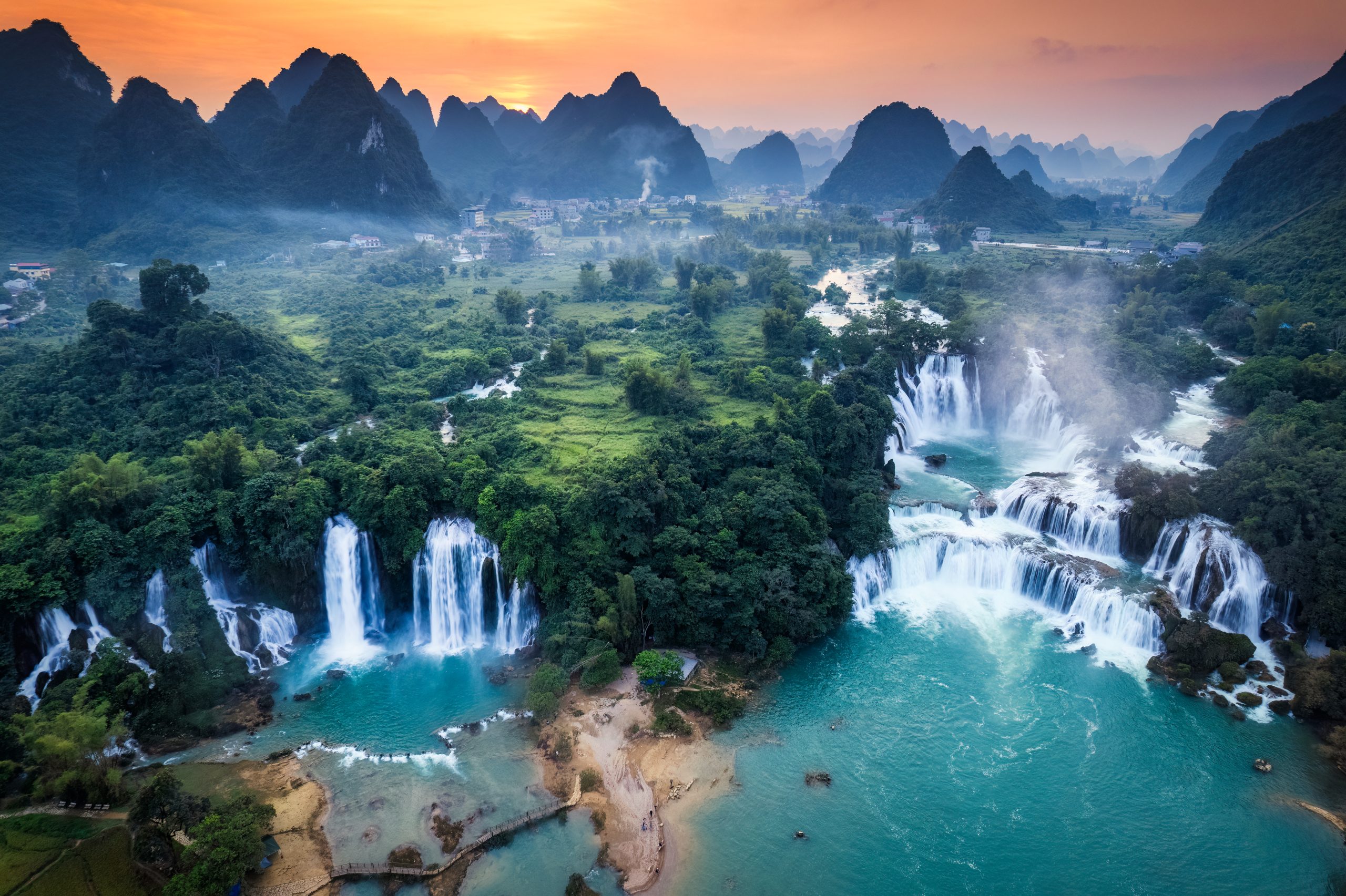 Panorama aerial view of sunset over mountain range with Ban Gioc waterfall or Detian Falls flowing in tropical rainforest at Cao Bang, Vietnam